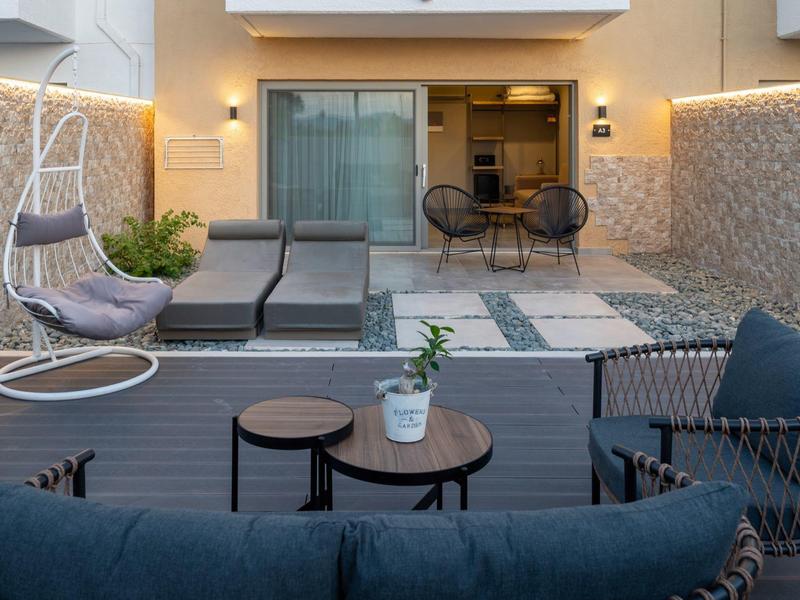 Moderní venkovní prostor se sezením, lehátky, závěsným křeslem a osvětleným bazénem.