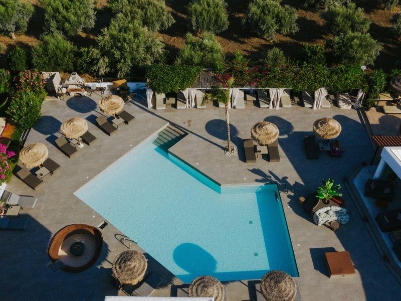 Pohled z ptačí perspektivy na bazén s deštníky obklopený stromy v hotelovém resortu.