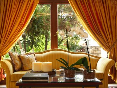 Gemütliches Wohnzimmer mit gelben Gardinen, Sofa und Tisch mit Kerzen und Pflanzen vor Fenster.