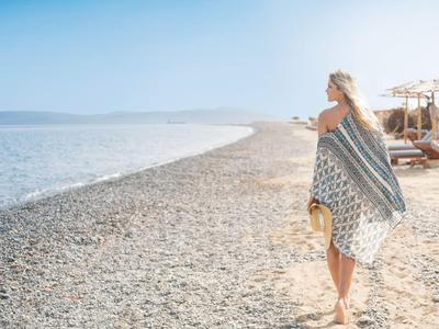 Frau mit Tuch am Kiesstrand mit Meerblick an einem sonnigen Tag.