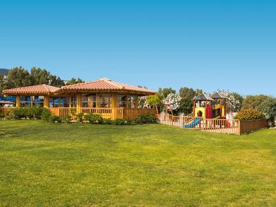 Ein einstöckiges gelbes Haus mit rotem Dach neben einem bunten Spielplatz und weitem grünen Rasen.
