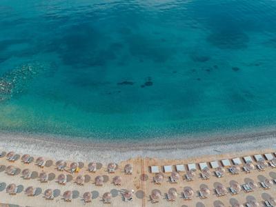 Strand mit Reihen von Sonnenschirmen und Liegestühlen am türkisblauen, klaren Meer.