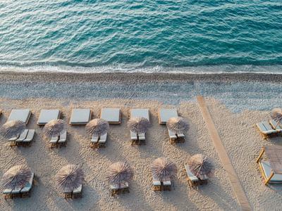 Luftaufnahme eines leeren Sandstrands mit Sonnenschirmen und Liegestühlen am ruhigen Meer.
