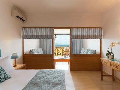 Schlichtes Schlafzimmer mit Holzbetten, blauem Kopfteil, Balkon und Meerblick im Hintergrund.