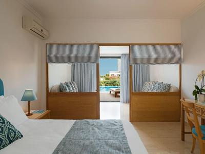 Modernes Schlafzimmer mit Doppelbett, Schreibtisch und Blick auf Terrasse mit Sitzbereich.