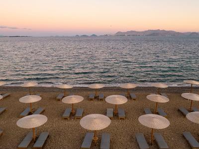 Leerer Sandstrand mit weißen Sonnenschirmen und Blick auf ruhiges Meer bei Sonnenaufgang.