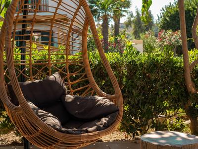 Gemütlicher Rattansessel mit Kissen in einem sonnigen Garten mit Palmen.