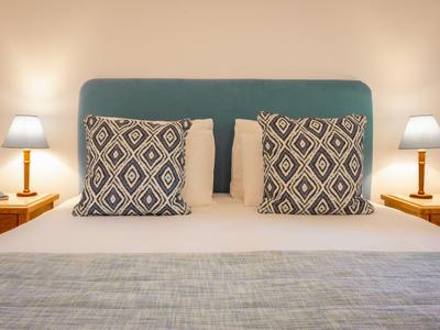 Hell beleuchtetes Hotelzimmer mit Doppelbett, gepolstertem Kopfteil und dekorativen Kissen.