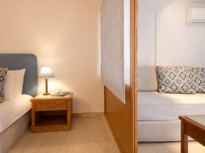 Zweibereich-Zimmer mit Bett, Sofabereich, Nachttisch und Lampe, neutralen Farben.