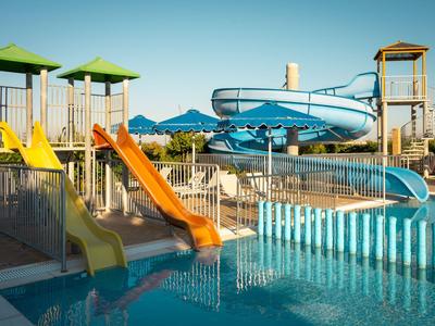 Leerer Hotel-Poolbereich mit Wasserrutschen und klares blaues Wasser bei Tageslicht.