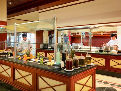 Buffet mit vielfältigen Speisen und Getränken in einem Hotelrestaurant mit Köchen im Hintergrund.