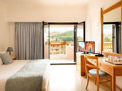 Hell eingerichtetes Hotelzimmer mit Balkon und Blick auf eine grüne Landschaft.