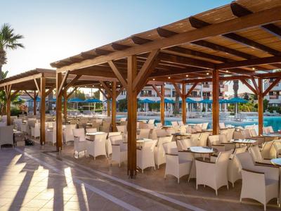 Freiluftrestaurant mit weißen Möbeln neben einem Pool in einem Hotelresort bei Sonnenuntergang.