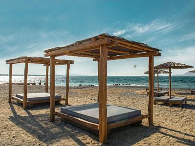 Strand mit hölzernen Schirmen und Betten auf Sand vor ruhigem Meer und blauem Himmel.
