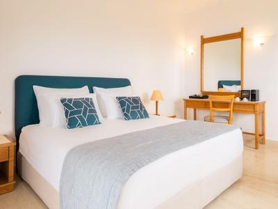 Hell eingerichtetes Hotelzimmer mit großem Bett, Nachttischen und Schreibtisch mit Spiegel.
