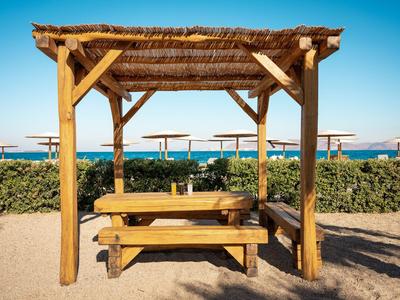 Holzbänkchen mit Überdachung am Strand mit Blick aufs Meer und Sonnenschirme im Hintergrund.