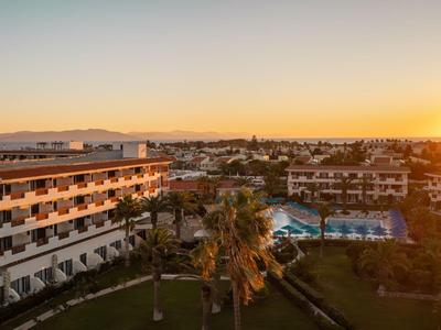 Großes Hotel mit Pool und Sonnenuntergang im Hintergrund in einer Urlaubsregion.