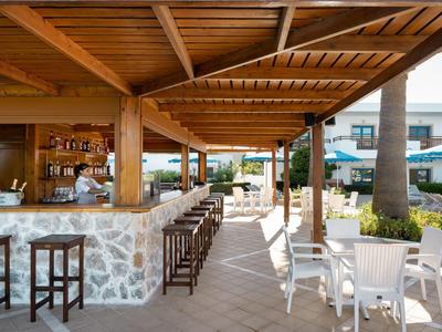 Überdachte Hotelbar mit Holzbalken, Stühlen und Tischen auf heller Terrasse bei Sonnenschein.