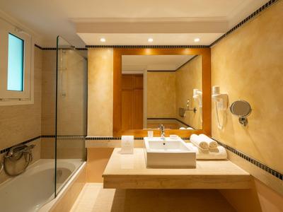 Modernes Badezimmer mit Badewanne, Waschbecken und gelblich-beigen Wänden in einem Hotelzimmer.