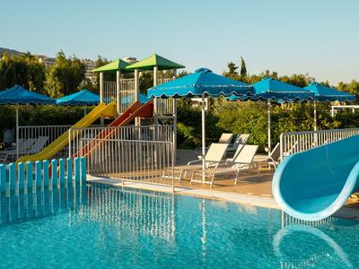 Poolbereich mit Wasserrutsche, Liegestühlen und blauen Sonnenschirmen im Sonnenlicht.