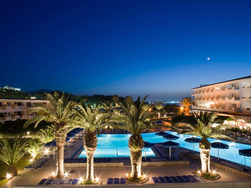 Beleuchteter Pool mit Palmen und Hotels bei klarer Nacht am Wasser.