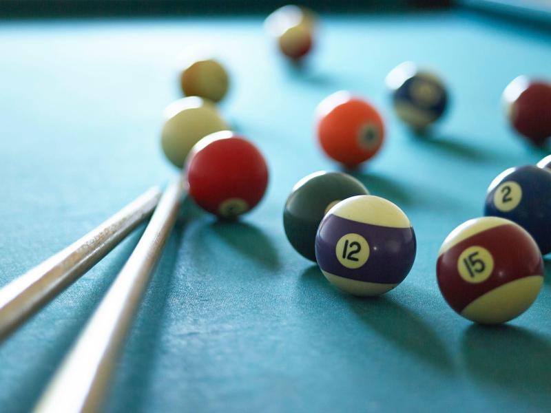 Blick auf Billardkugeln und Queues auf einem blauen Billardtisch.