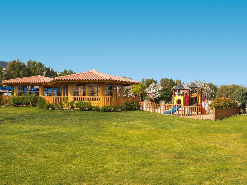 Ein einstöckiges gelbes Haus mit rotem Dach neben einem bunten Spielplatz und weitem grünen Rasen.