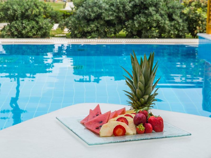 Ein Teller mit Ananas, Wassermelone und Erdbeeren vor einem blauen Swimmingpool.