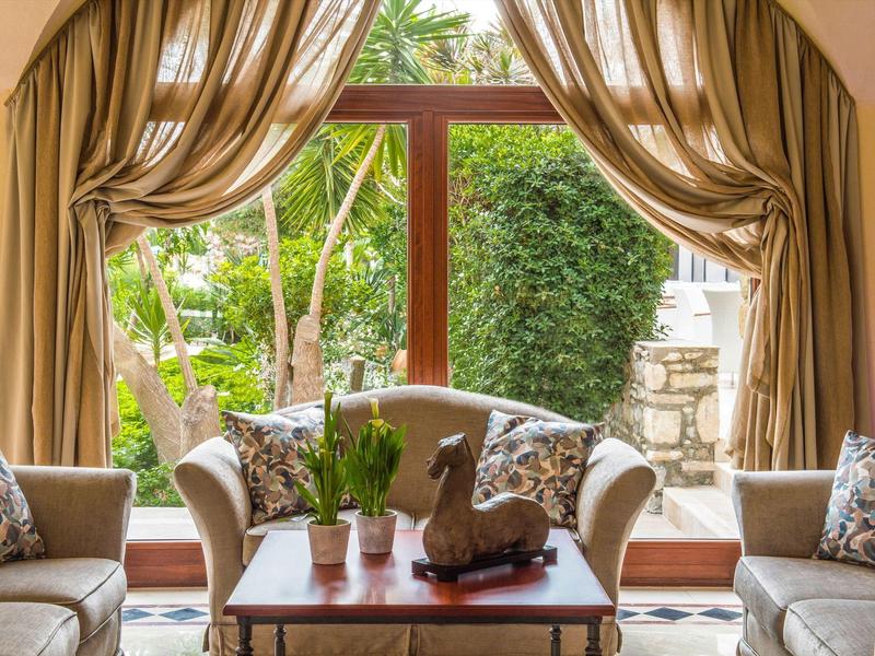 Gemütliches Wohnzimmer mit hellbraunen Vorhängen, Sofas und Tisch vor großem Fenster zum Garten.