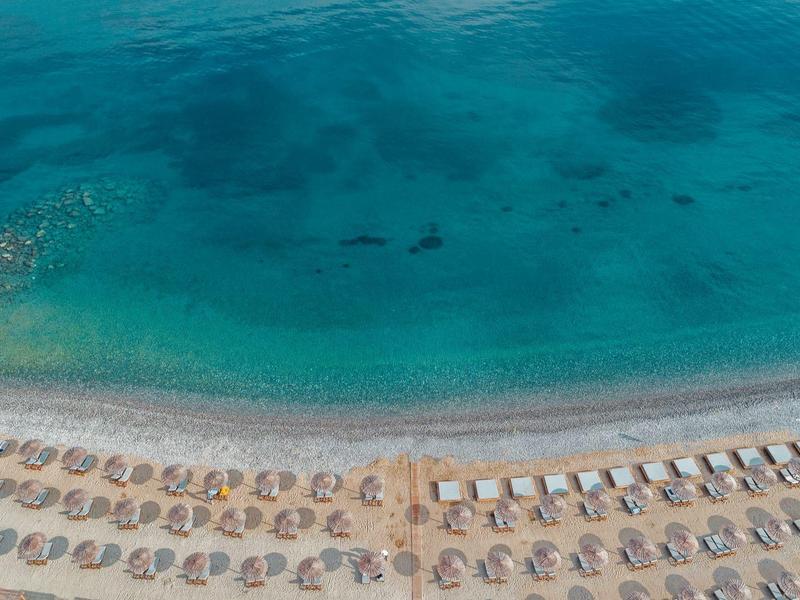 Strand mit Reihen von Sonnenschirmen und Liegestühlen am türkisblauen, klaren Meer.