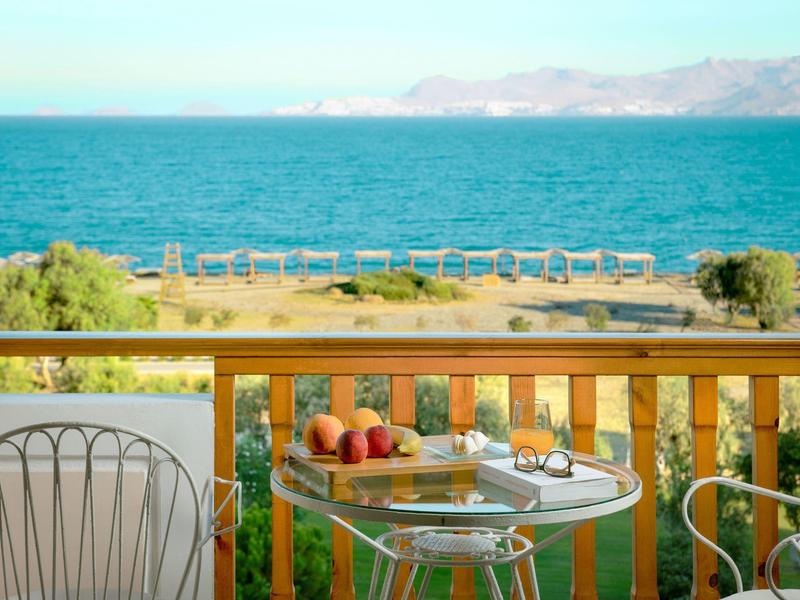 Balkon mit Glas und Äpfeln, Stühlen, Blick auf blaues Meer und entfernte Berge bei klarem Himmel.