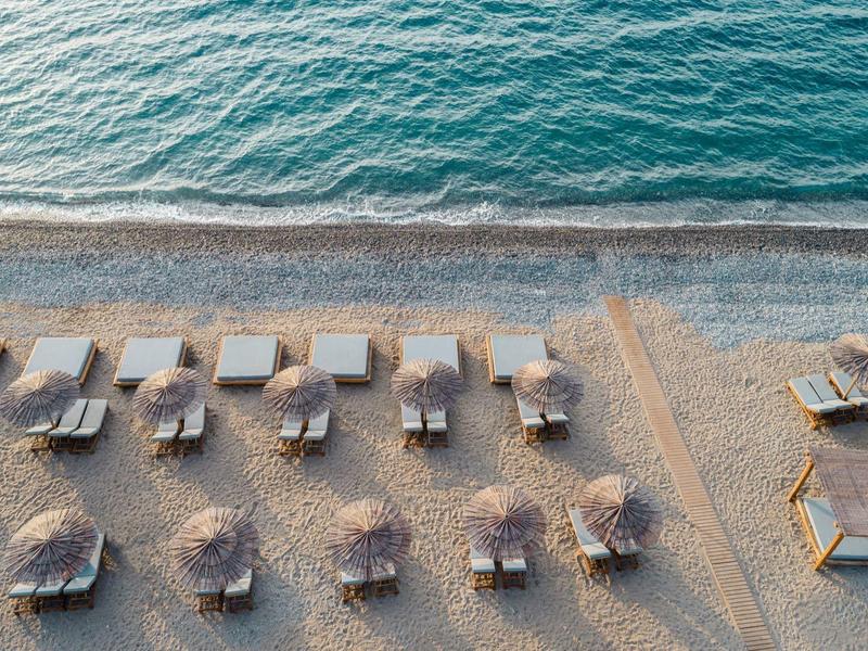 Luftaufnahme eines leeren Sandstrands mit Sonnenschirmen und Liegestühlen am ruhigen Meer.