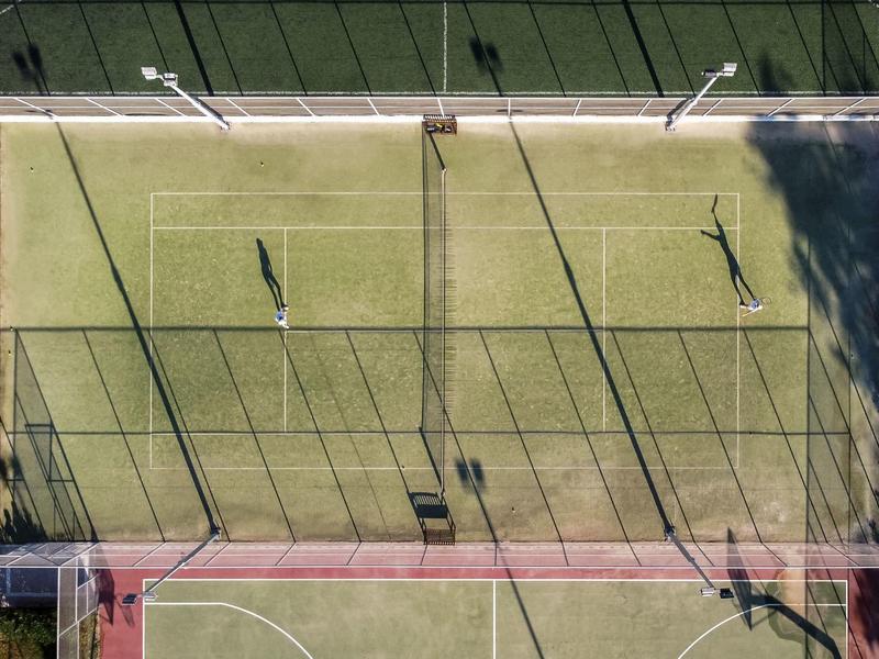 Luftaufnahme eines Tennisplatzes mit zwei Spielern und langen Schatten bei Sonnenlicht