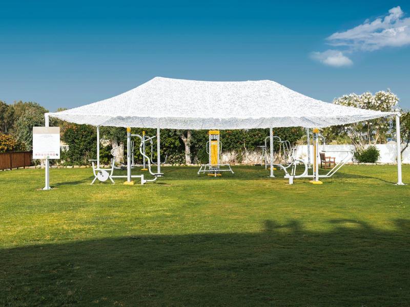 Weißes Sonnensegel mit Metallgestell auf grünem Rasen unter blauem Himmel.