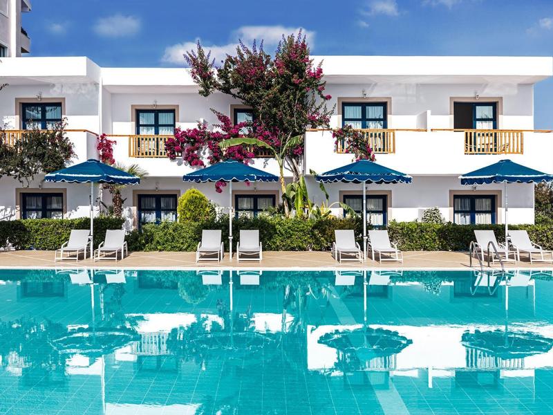 Moderner weißer Gebäudekomplex mit blauen Sonnenschirmen und türkisfarbenem Schwimmbad.