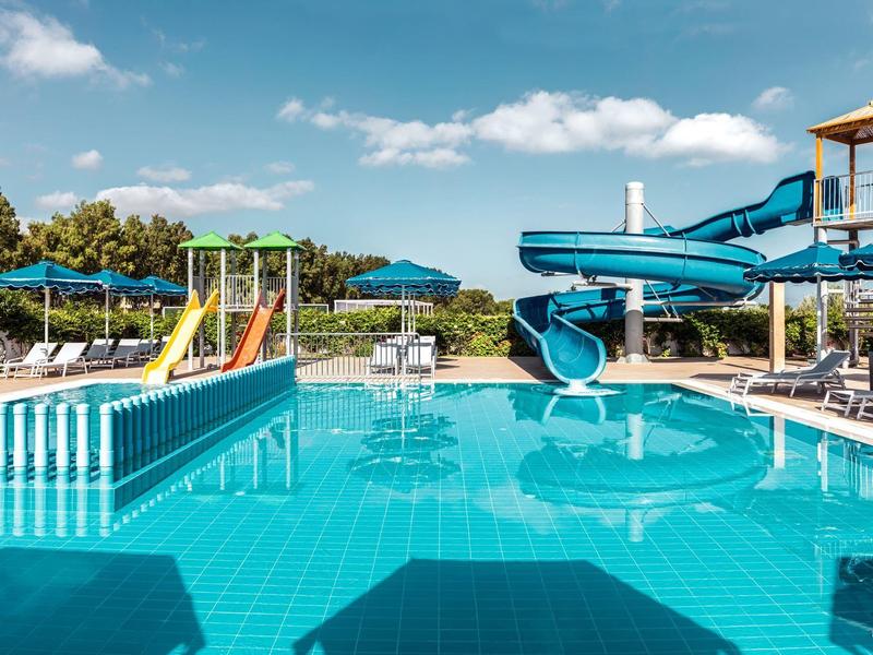 Schwimmbad mit Wasserrutsche, Liegestühlen und Sonnenschirmen bei blauem Himmel.