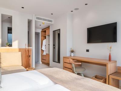 Modern ausgestattetes Hotelzimmer mit Doppelbett, Schreibtisch, Fernseher und Sitzbereich in hellen Farben.