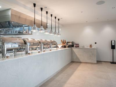 Nowoczesna kuchnia hotelowa z stalową stacją serwowania i białym blatem pod lampami wiszącymi.