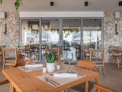 Modernes Restaurant mit Holztischen und Steinwänden, dekoriert mit Pflanzen.