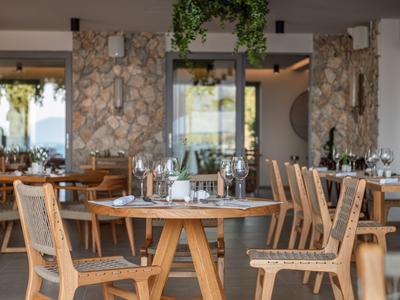 Elegantes Restaurant mit Holztischen und Stühlen sowie Fenstern mit Blick auf grüne Landschaft.