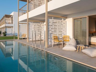 Hotel moderno con piscina e terrazza, arredato con sedie e cuscini sotto una luce calda.