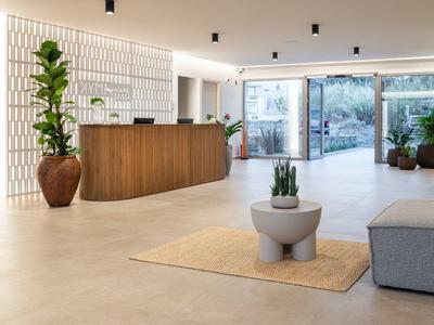 Jasne lobby hotelowe z drewnianą recepcją, dużymi roślinami i nowoczesnym miejscem do siedzenia.