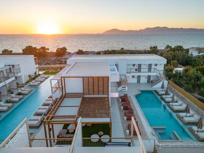 Nowoczesny kompleks hotelowy z dwoma długimi basenami, leżakami i widokiem na morze o zachodzie słońca.