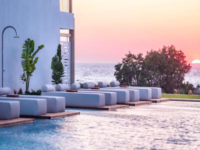 Moderne Lounge-Betten am Pool mit Blick auf den Sonnenuntergang am Meer.