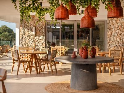 Gemütliche Terrasse mit Steinhaus, Holztischen und Stühlen, Dekoration mit Pflanzen und Vasen.