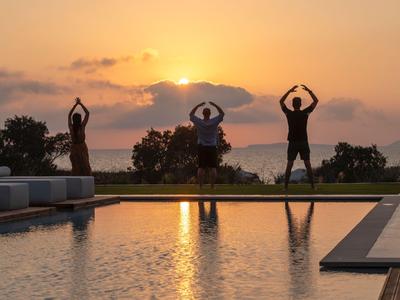 Drei Personen praktizieren Yoga am Pool bei Sonnenuntergang mit Blick auf das Meer.