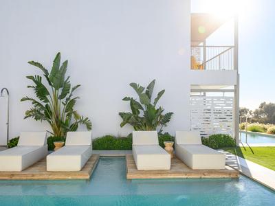 Moderne Außenpool-Lounge mit weißen Liegen und Pflanzen neben einem weißen Gebäude.