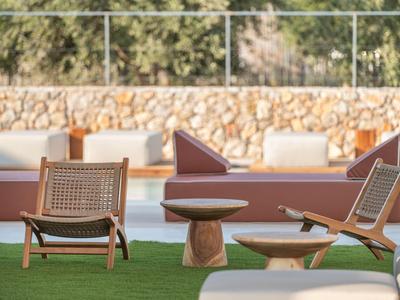 Zwei Stühle und ein Tisch auf grünem Rasen vor einem Pool und einer steinernen Mauer.