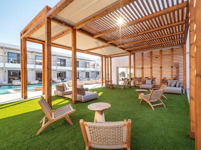 Überdachte Lounge mit Holzpergola, Sitzgelegenheiten und Blick auf den Pool und Gästezimmer.