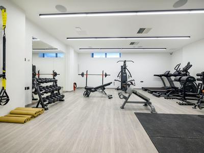 Moderner Fitnessraum mit verschiedenen Trainingsgeräten und hellem Holzboden.
